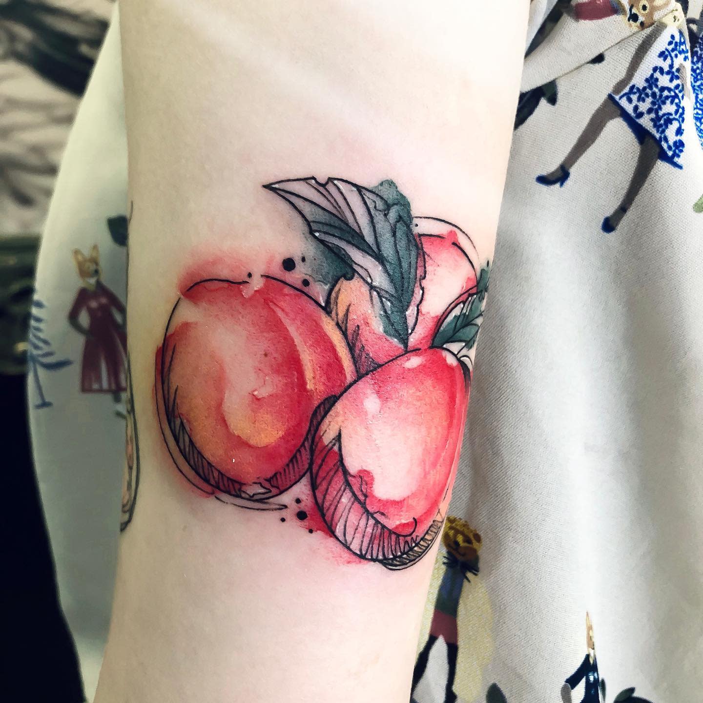 A colorful tattoo of three peaches with leaves on an arm